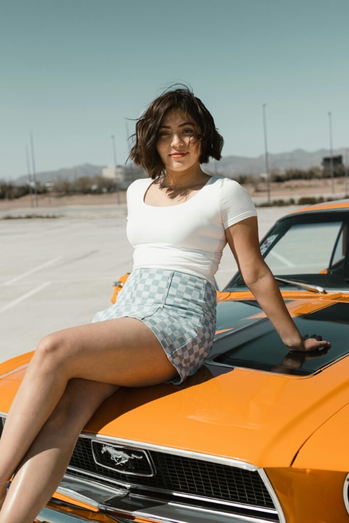 Stylish woman posing on a classic orange Ford Mustang in sunny Los Angeles.